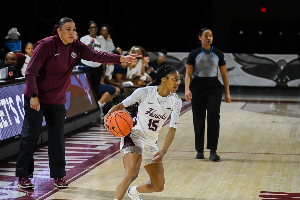 Kalise Hill brings the ball up the floor as head coach Malikah Willis points at a spot on the floor.