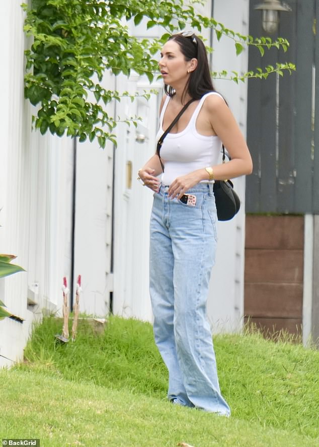 Her dark hair was worn straight and tucked behind her ears, with sunglasses perched on her head, as she appeared preoccupied while standing on the grass outside the home