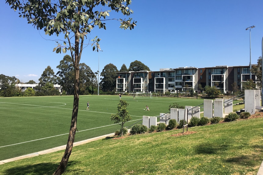 footballers play on a green synthetic turf field among apartments
