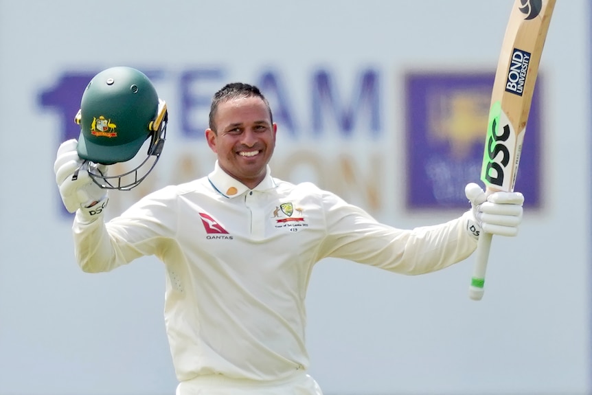 Usman Khawaja raises his bat and helmet in celebration