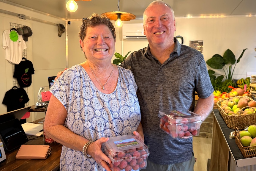 A smiling Leonie and Cliff holding lychees in a farm shop.