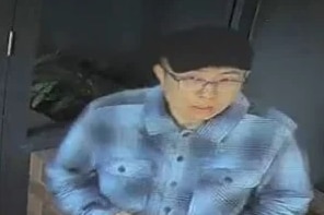 A man wearning a blue longsleeve shirt, black hat, glasses and tan shorts.