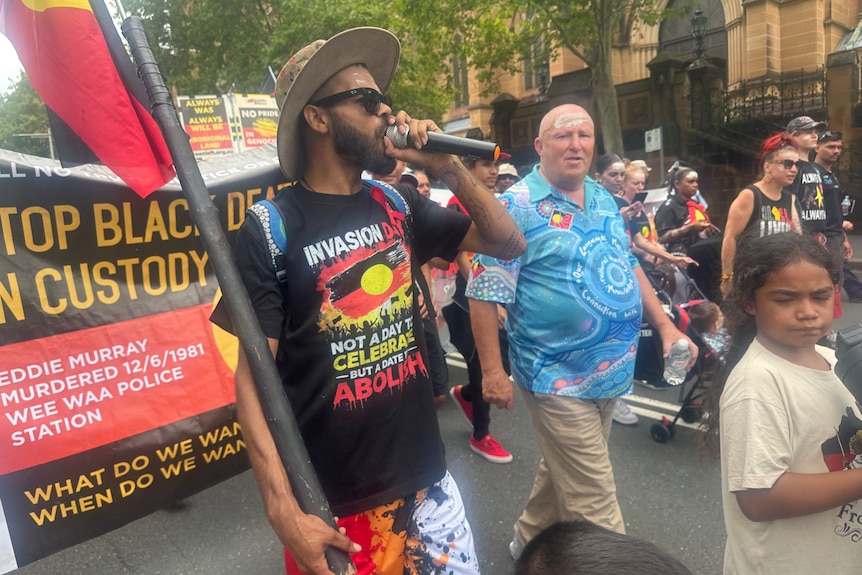A man with a microphone carrying an Aboriginal flag