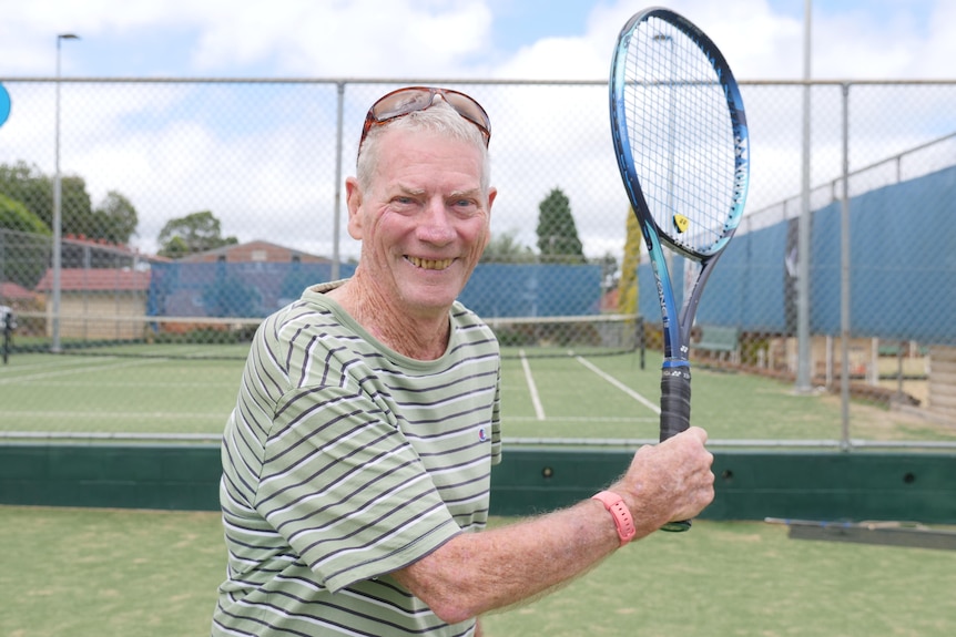 man in his 80s smiling holding a tennis racquet