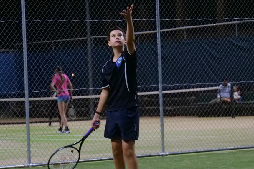 teenage boy serving a ball on a tennis court