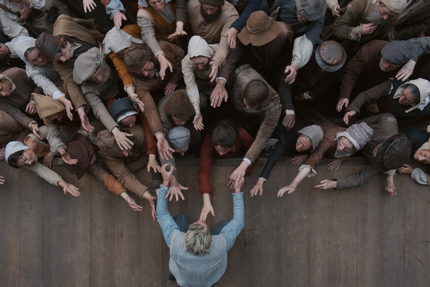 A boy reaches for the crowd on a stage while the crowd reaches back