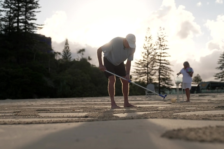Man raking patterns in the sand on the beach as the sun rises.