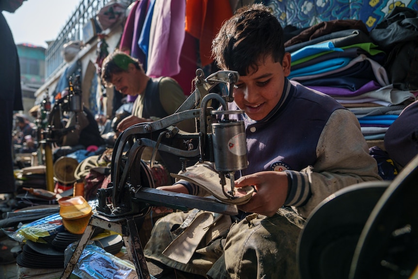 An Afghan boy sews a piece of material on a machine in a busy market in Kabul.