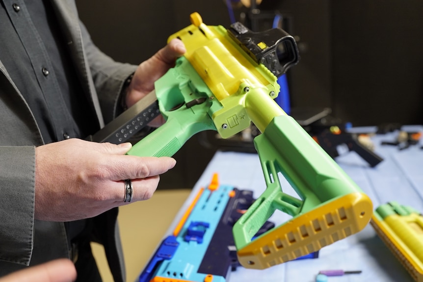 A man holds a green 3D-printed gun.