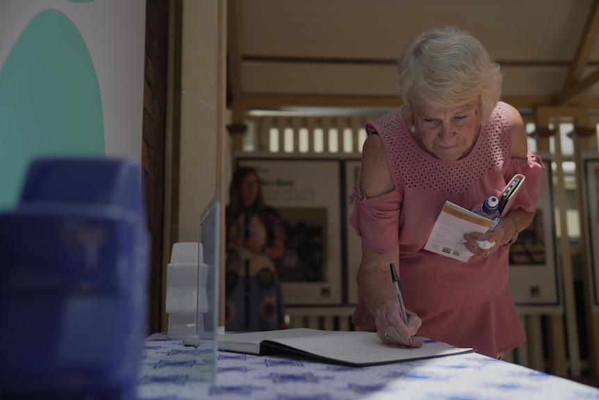 A woman leans down to write in a book.
