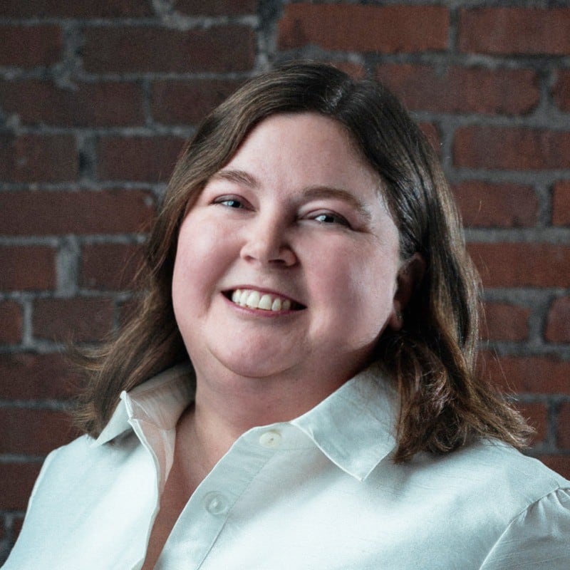 A white woman with dark brown hair, she is wearing a white shirt.