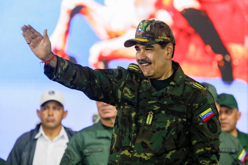 A middle-aged man in fatigues with a thick black mustache waves to a crowd.