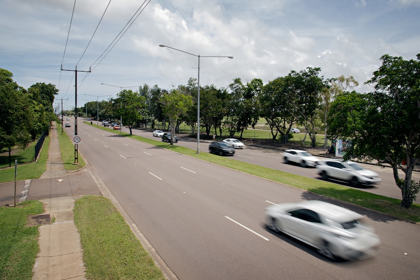 Cars travelling on a busy road, surrounded by grass and trees. 
