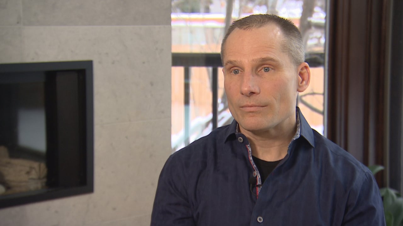 A man in a blue shirt sits in front of a window.