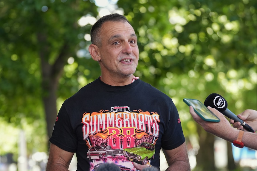 A man speaks enthusiastically at a press conference outdoors.