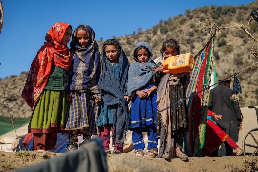 A line of girls stand together wearing hijabs in an Afghan camp.