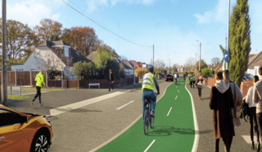A CGI image of Woodlands Avenue, with cyclists using a distinctive marked green cycle path which is divided into two paths, a runner on a pavement opposite and people walking on a pavement closer. An orange car is driving just behind the cyclist.