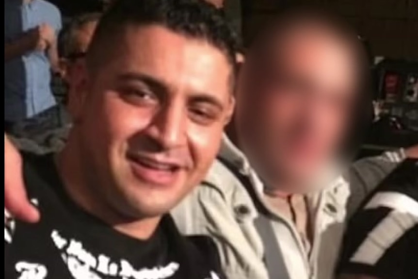 Kazem Hamad wearing a black T-shirt sitting next to two unidentified men with their faces blurred.