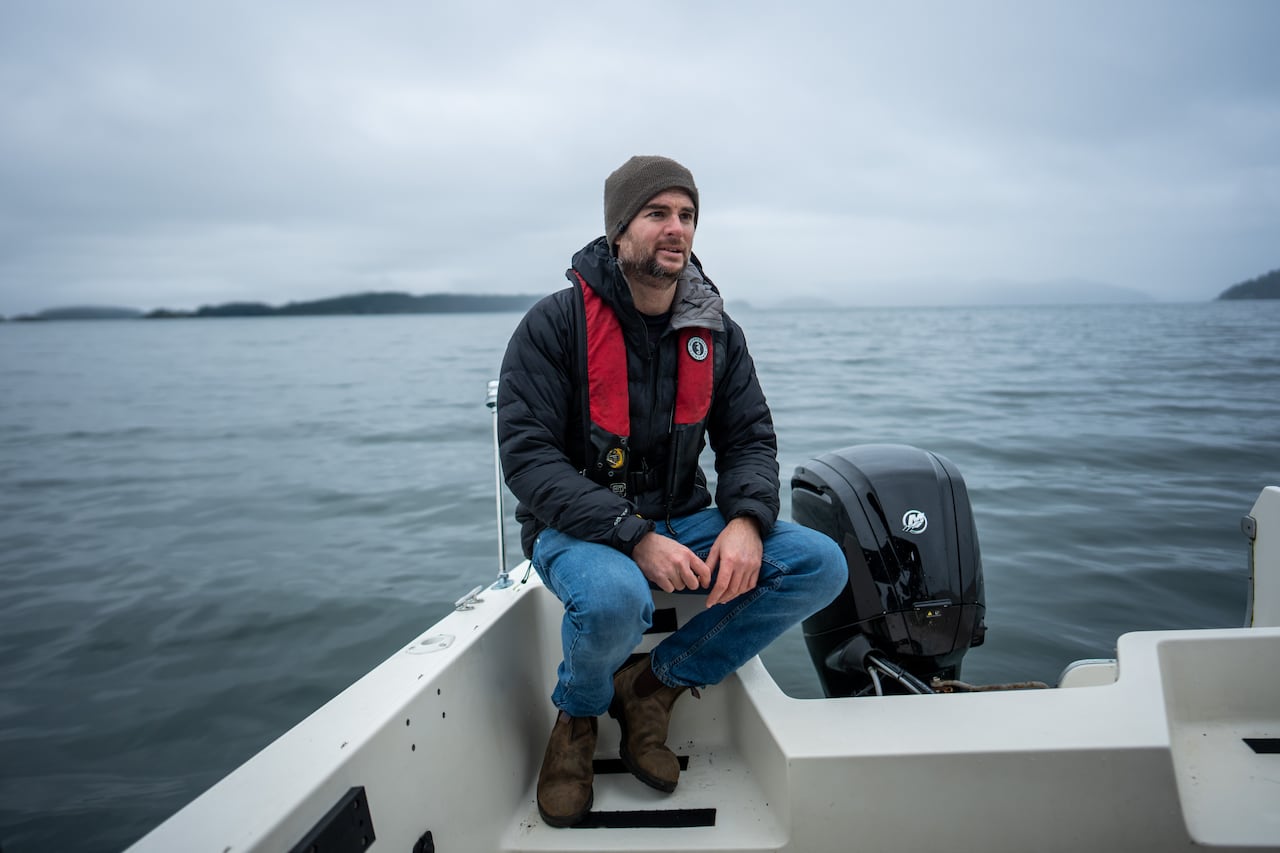 A man perches on the edge of a boat on a cloudy day.