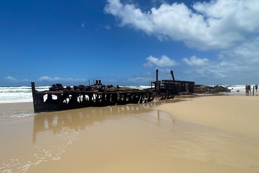 An old rusted shipwreck embedded in sand surrounded on one side by water