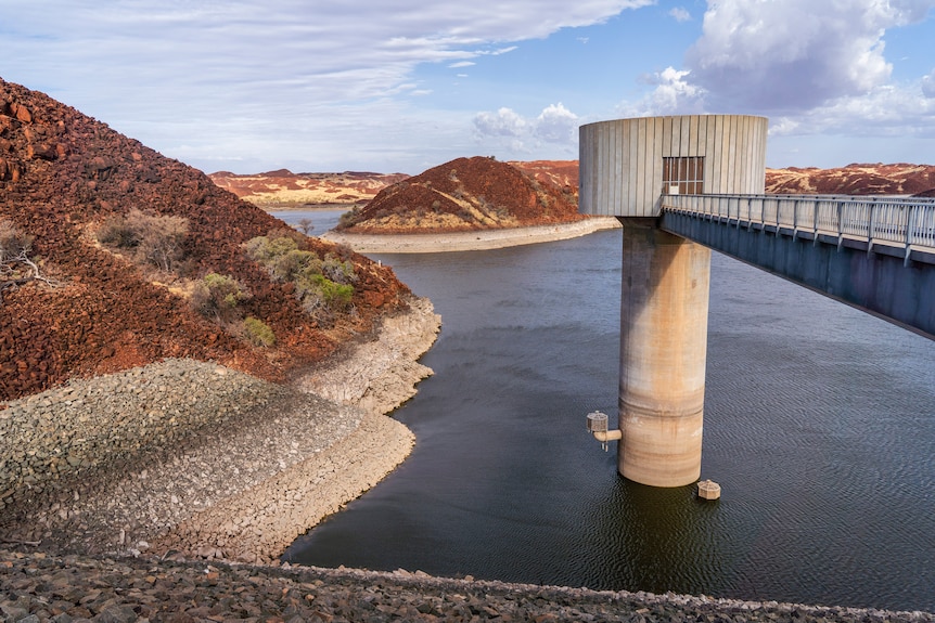 A bridge connects to a tower in an outback dam surrounded by rugged countryside.