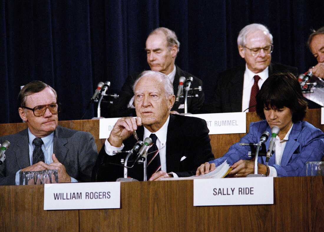 Seated in front of microphones, the chairman of the Presidential Commission on the Space Shuttle Challenger Accident, William Rogers (center), and panel members Neil Armstrong (left) and Sally Ride (right) attend one of the hearings concerning the disaster, on February 25, 1986, in Washington, D.C.