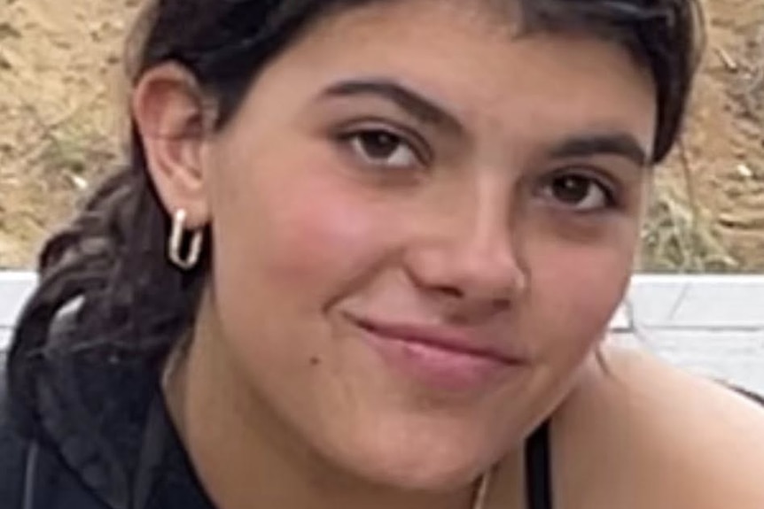 A close up of a young woman with dark hair, smiling.