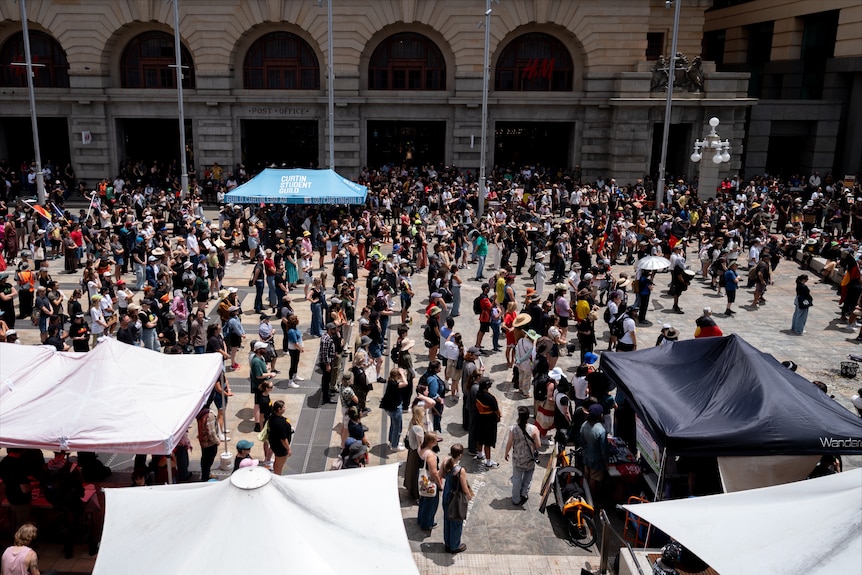 Hundreds of people gather in Perth's CBD with stone arched buildings surrounding them.