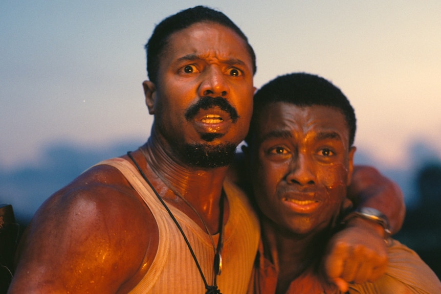 Two black men, one with his arm around the other, looking fearfully at something in the distance