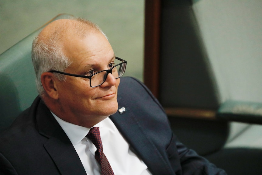 A middle-aged man in glasses — former prime minister Scott Morrison — wears a dark suit as he sits in parliament.