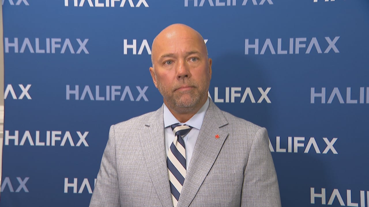 Man in suit stands against a blue wall with "Halifax" written on it
