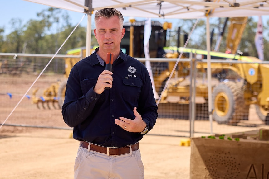 A man speaking in front of a construction site with machinery in background