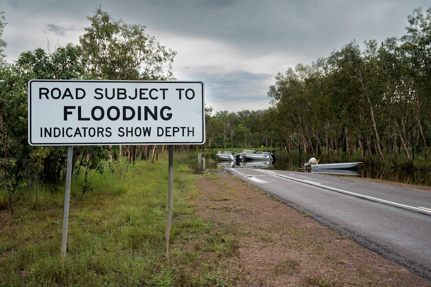 A sign near a flooded road in a national park reads: road subject to flooding, indicators show depth.