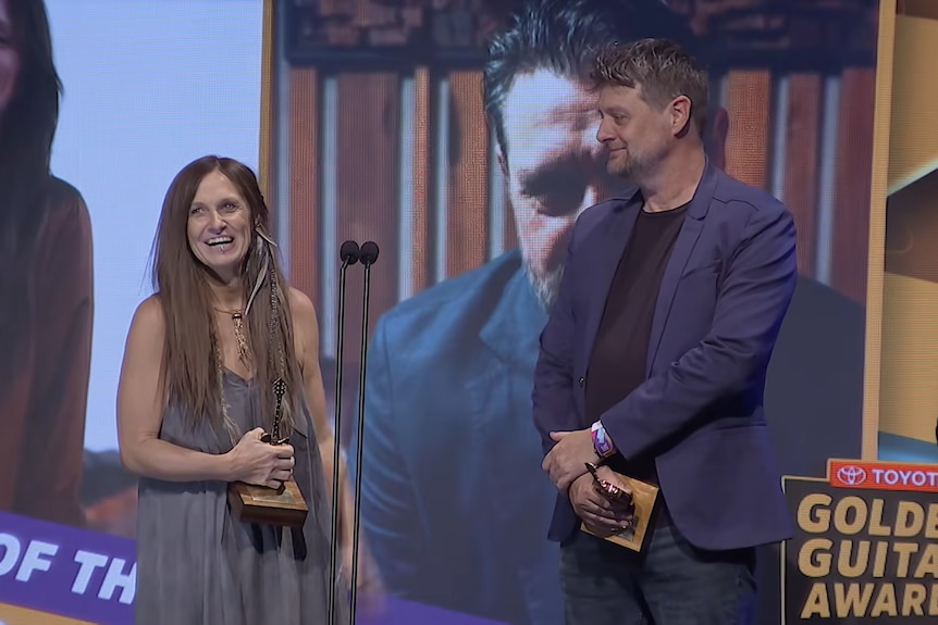 A man and woman on stage holding golden guitar awards