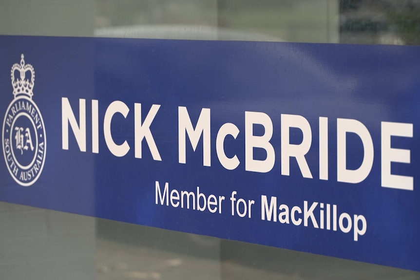 A blue sign on glass that reads 'Nick McBride Member for MacKillop'. 