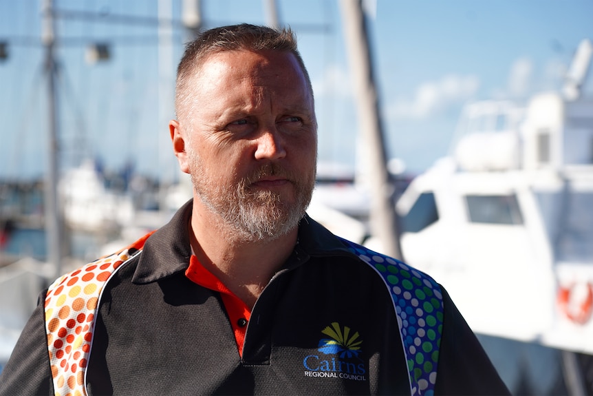A man wearing a Cairns council t-shirt in front of a boat jetty.