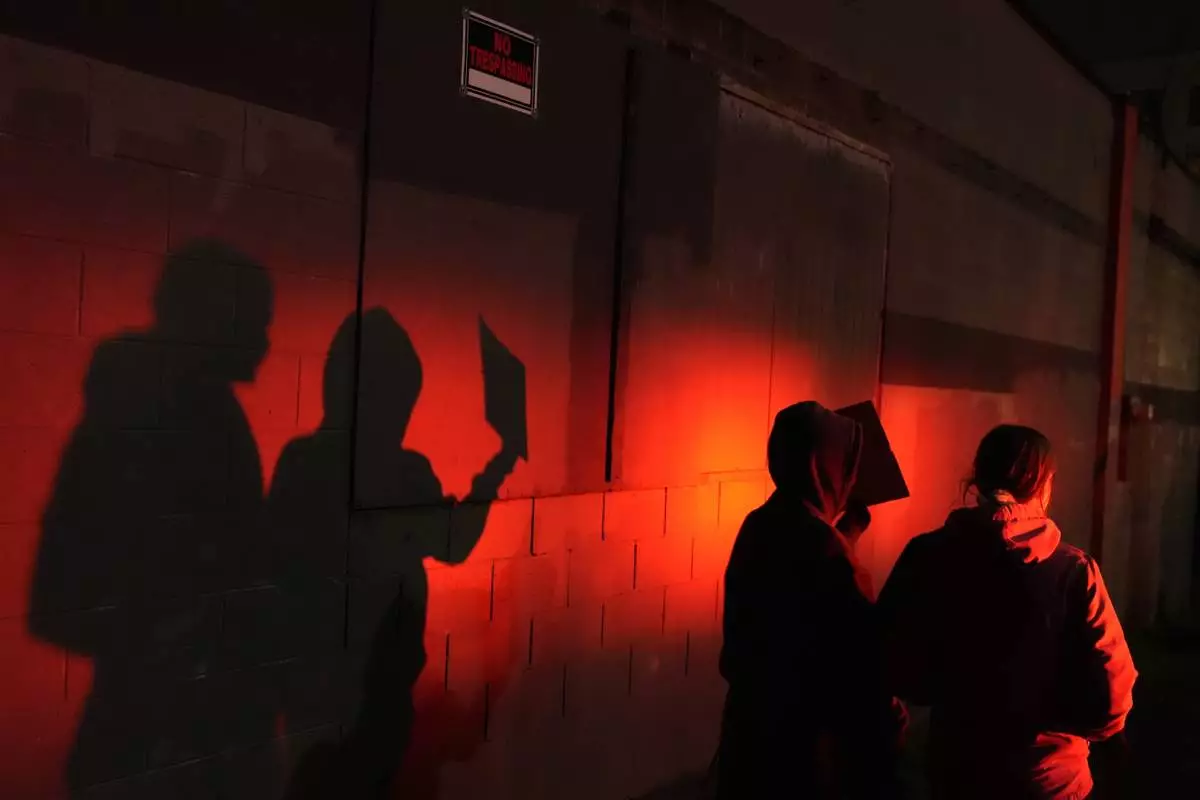 Two protesters are lit by a police light as they walk outside the U.S. Immigration and Customs Enforcement facility on Thursday, Jan. 8, 2026, in Portland, Ore. (AP Photo/Jenny Kane)