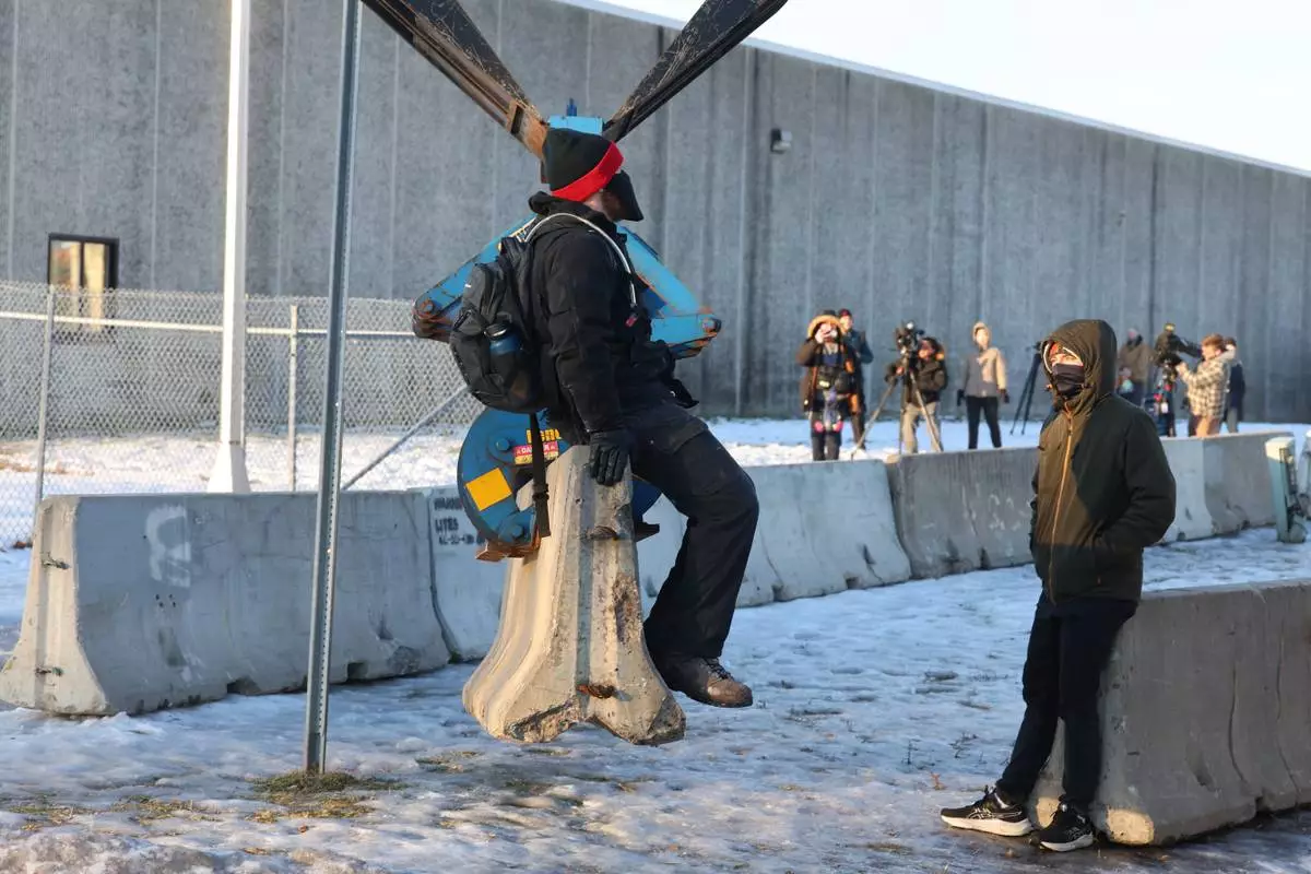 Protesters sit on a barrier that is being assembled outside the Bishop Henry Whipple Federal Building as protesters gather in Minneapolis, Friday, Jan. 9, 2026. (AP Photo/Adam Bettcher)
