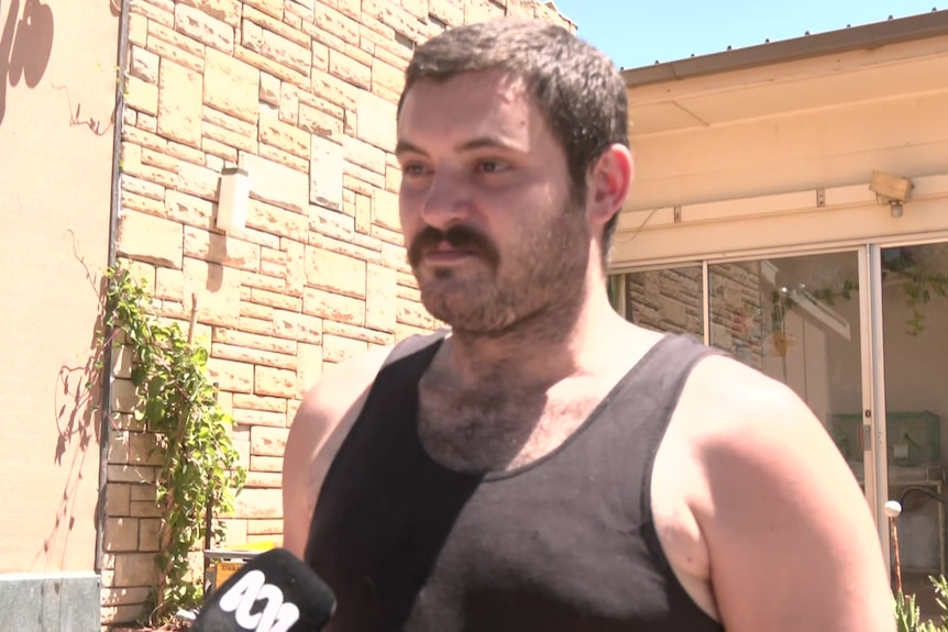 A man with a black singlet stands in front of his house