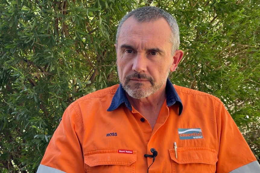 Ross Berry wears an orange Essential Water shirt as he sits in front of a hedge, looking just off camera 
