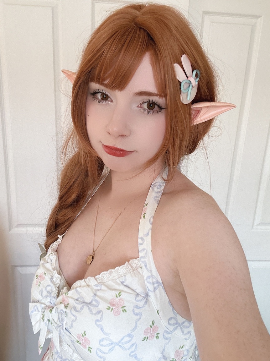 A close up of a woman's face, she has auburn hair and wears pixie ears. 