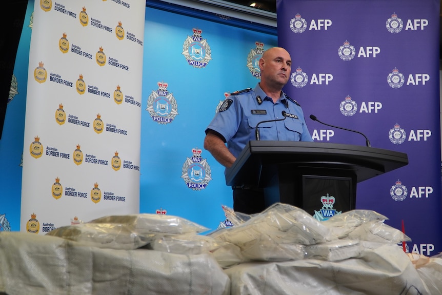 A WA Police officer stands in front of a large haul of drugs in plastic bags. 