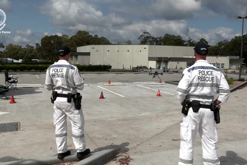 Two police officers in white uniforms stand in car park operating a drone.