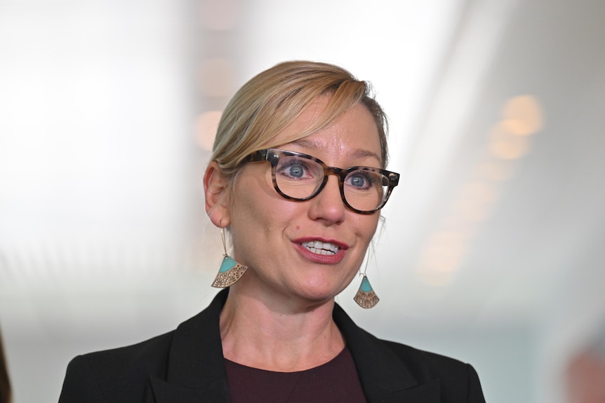 A blonde haired woman wearing glasses speaks