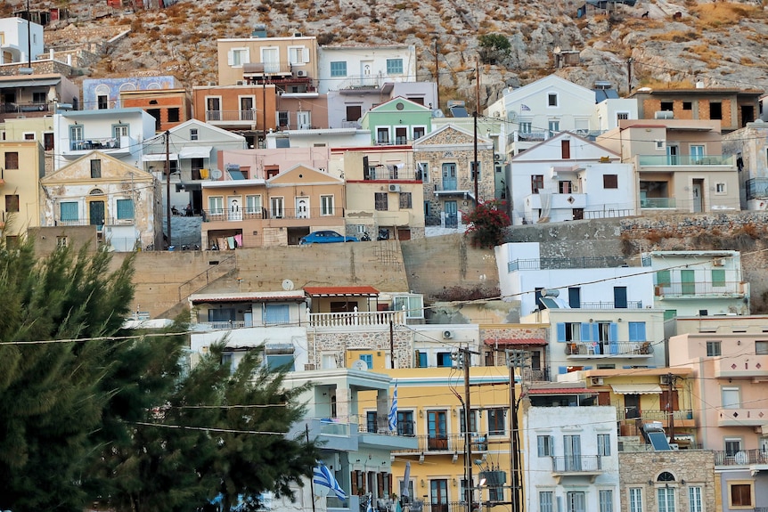 A number of colourful, pastel coloured greek-styled homes built onto a cliff edge.