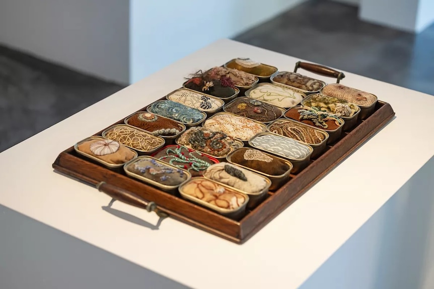 A textile artwork featuring a series of handmade sardine cans, each filled with different elements