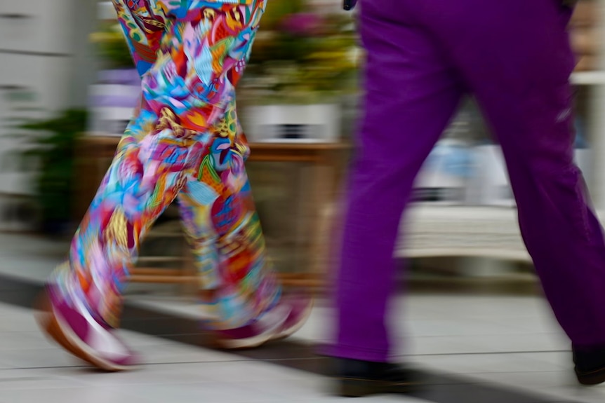The blurring legs of two people in scrubs. The person on the left is wearing rainbow swirled pants. the one on the right's pa