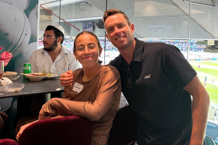 Mr Doolan with one arm around Chaya in a suite watching the cricket down below at the SCG.