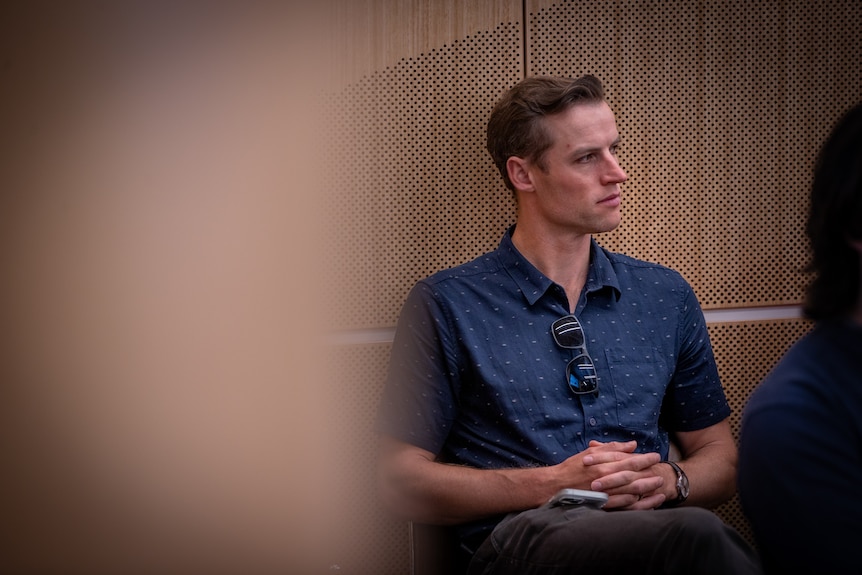 A man in a blue shirt sitting down on a chair.