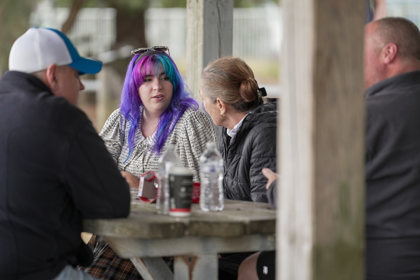 A group of people sitting around a table at a park.